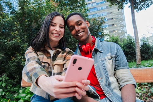 Preview: A young multiracial couple enjoys browsing the internet on a cellphone. Two teenage friends use a