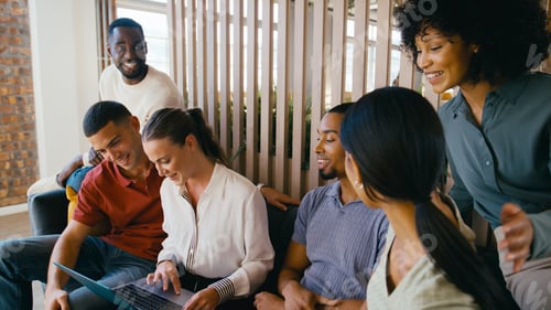 Preview: Multi-Cultural Business Team Sitting On Couch In Modern Open Plan Office Working On Laptop Together