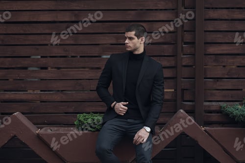 Preview: Fashionable man, wearing a suit, sitting against the wooden wall