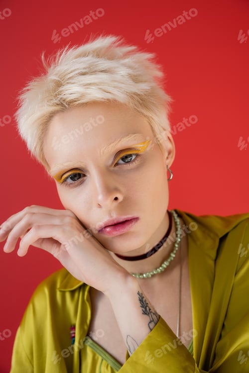 Preview: portrait of tattooed woman with bright eyeliner looking at camera on carmine pink