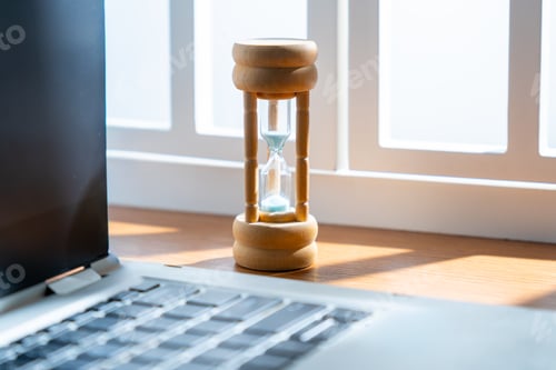 Preview: A close-up of a small hourglass next to a laptop.
