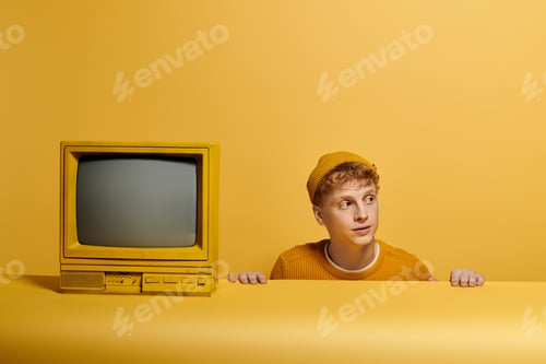Preview: A young man with vibrant red hair showcases a fashionable winter outfit near vintage television