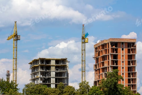 Preview: Apartment buildings under construction. Tower cranes on blue sky copy space background