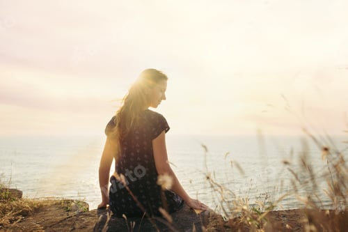 Preview: Woman sitting on the cliff on sunset background