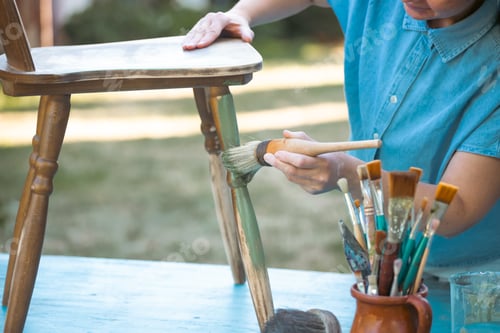 Preview: Woman painting a wooden furniture outdoors, an eco-friendly re-use business.