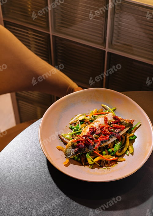 Preview: Grilled sea bass fillet with sauteed vegetables on restaurant table