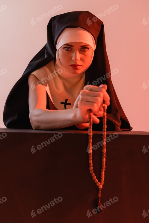 Preview: young nun looking at camera while holding prayer beads isolated on pink