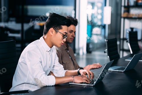 Preview: side view of multicultural businessmen working at table with laptops at modern office