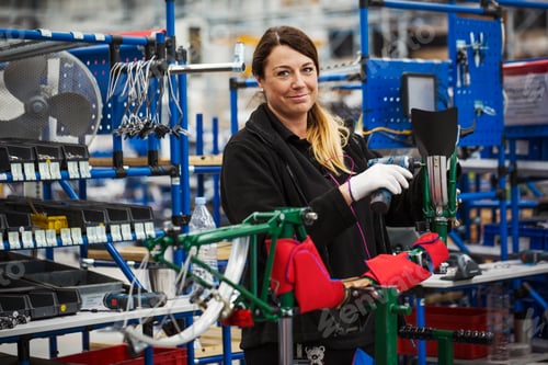 Preview: Female skilled factory worker assembling a bicycle in a factory working on the frame and wheels.
