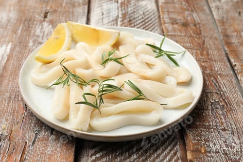 Preview: Uncooked squid rings with lemon slices and rosemary on wooden table, closeup