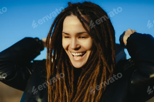 Preview: Young caucasian female with dreadlocks smiling outdoors in clear blue sky