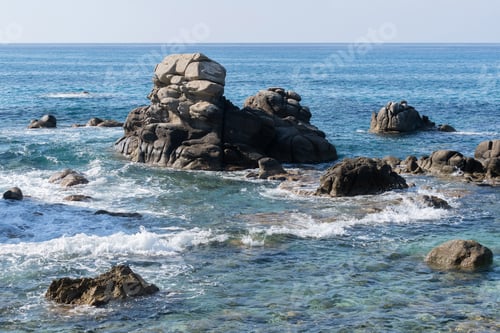 Preview: Wild rocky beach coastline and the sea, wave splashes on rock in sea shore, calm sea. Breaking waves