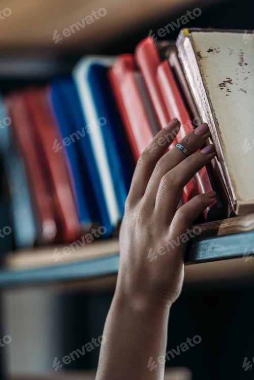 Preview: Cropped shot of student holding book at bookshelf in library