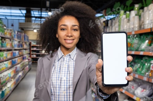 Preview: In a supermarket aisle, an African American woman smiles while holding a smartphone with a blank