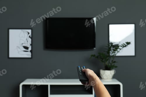 Preview: Woman switching channels on plasma TV with remote control at home