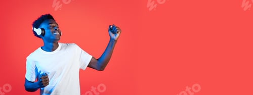 Preview: Young man dances joyfully with headphones against a vibrant red background