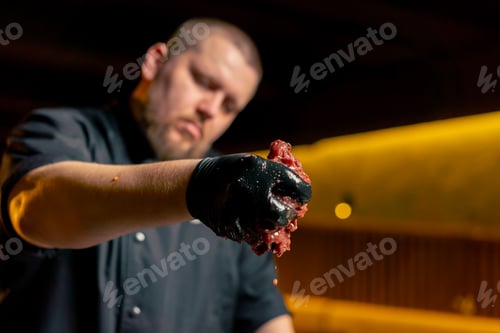 Preview: close up in a restaurant in a rib bar in the central hall a chef in black gloves sprinkles raw pork