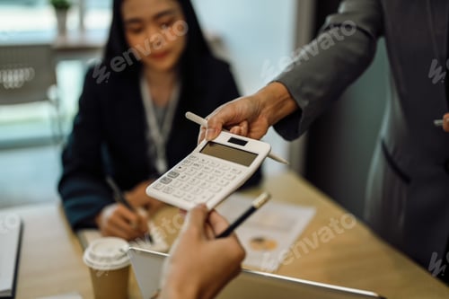 Preview: Female team leader showing finances or calculations on a calculator to colleagues in a meeting.