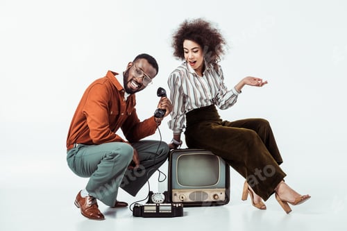 Preview: happy african american retro styled couple with vintage television and phone on white