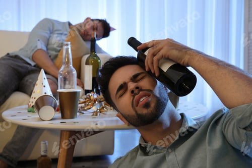 Preview: Young man suffering from hangover in messy room after party