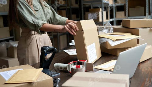 Preview: Female small business owner packing ecommerce order package in box at table.