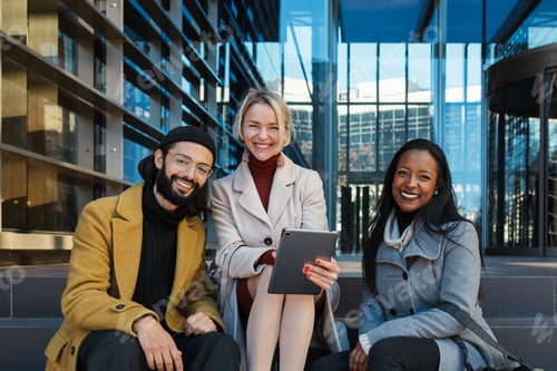 Preview: Business colleagues looking at camera and smile while sitting on the stairs outside the office