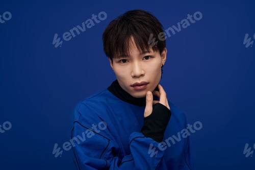Preview: Young handsome Asian man posing thoughtfully against a vibrant blue backdrop