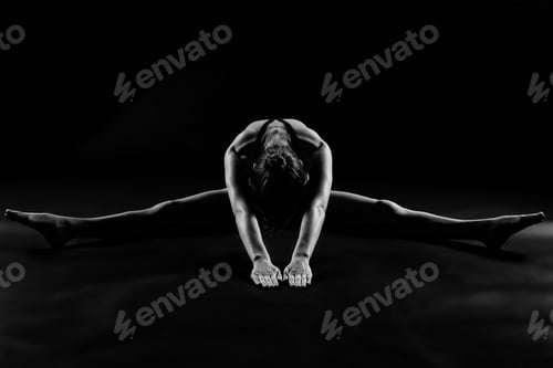 Preview: Grayscale shot of a woman in sportswear doing yoga in a studio with a dark background