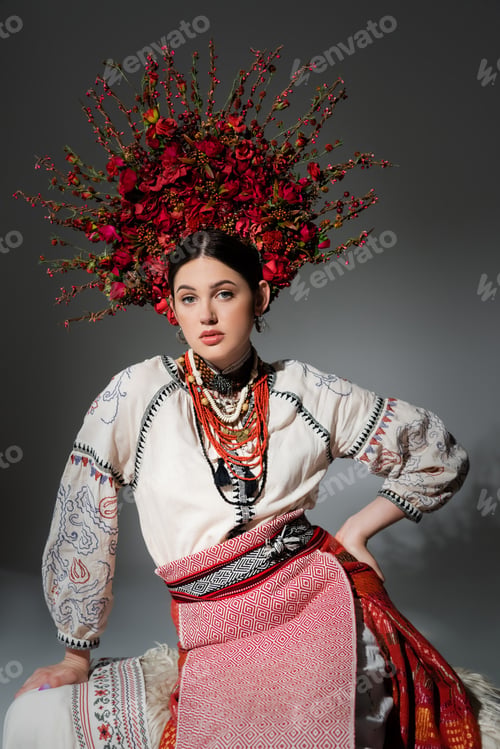 Vista previa: pretty ukrainian woman in traditional clothes and red wreath with flowers posing with hand on hip on