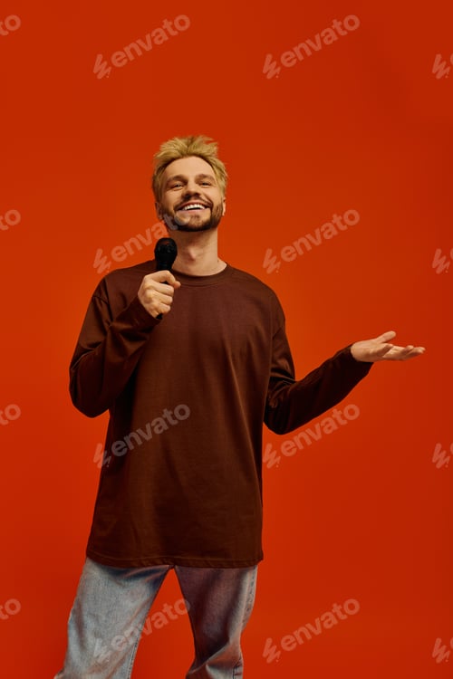 Preview: Handsome young man performs on stage against a vibrant orange backdrop with enthusiasm