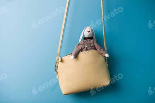 Preview: Handmade rabbit toy - a soft bunny sits in a women's handbags against a blue wall.