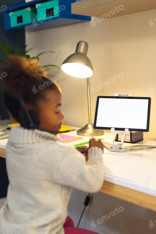 Preview: Vertical picture of happy african american girl learning, using tablet at home
