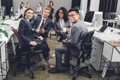 Preview: young multiethnic businesspeople in formal wear sitting together and smiling at camera in office