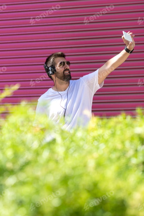 Preview: Bearded man with sunglasses taking a selfie against pink wall