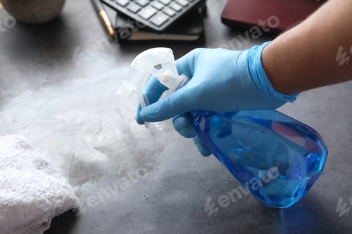 Preview: hand in blue rubber gloves holding spray bottle cleaning table