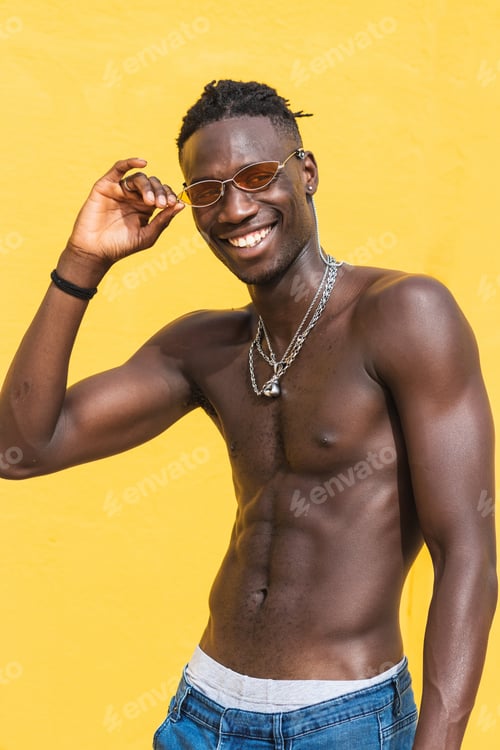 Preview: Portrait of a young man shirtless with sunglasses, isolated on yellow