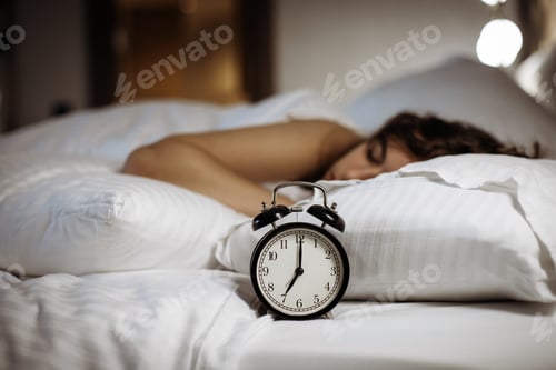 Preview: Alarm clock on the bed with sleeping woman behind. Seven o clock in the morning