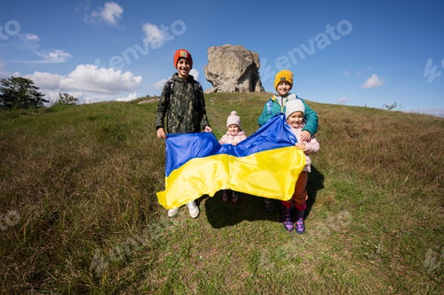 Preview: Welcome to Ukraine. Four children hold ukrainian flag near big stone in hill Pidkamin.