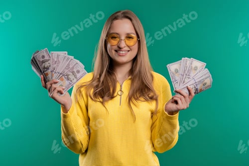 Preview: Rich excited blonde woman with cash money USD currency dollars banknotes on teal