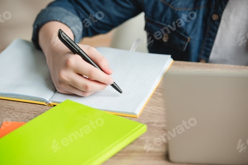 Preview: cropped view of schoolboy writing in notebook while doing schoolwork at home