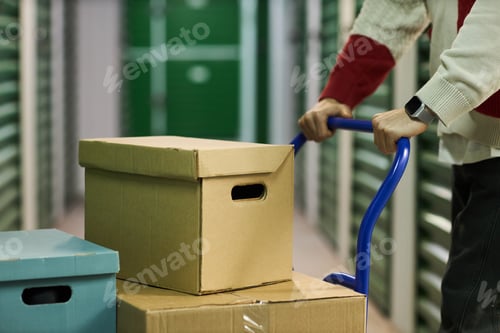 Preview: Young Adult Man Pushing Cart with Cardboard Boxes in Storage Facility