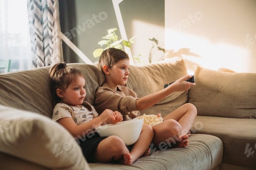Preview: kids are sitting on the couch, watching TV and eating popcorn