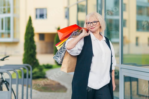 Preview: Portrait of beautiful senior woman goes happy holding shopping, paper colored bags, gifts, shopping