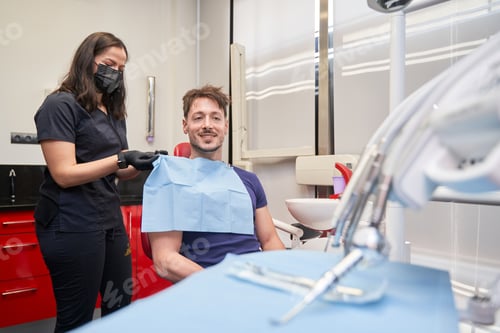 Preview: latina woman dentist putting a bib on a smiling man sitting in the chair to perform a procedure