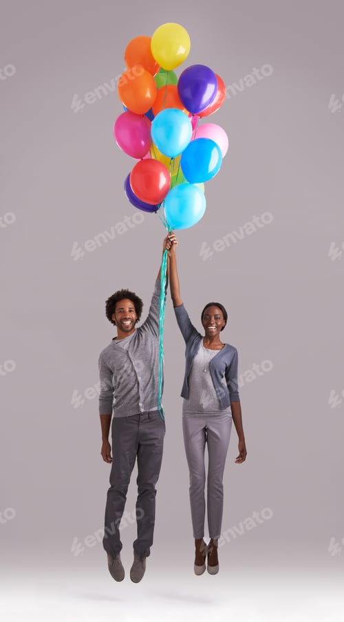 Preview: Lets fly away. Studio shot of a young couple holding a bunch of balloons as they float away.