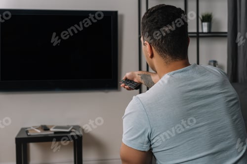 Preview: back view of mixed race man holding remote controller near flat panel tv with blank screen
