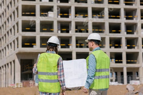 Preview: engineers hold in their hands a large work plan on paper and discuss the progress of construction.
