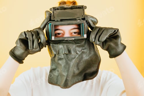 Preview: Young woman with a welder mask, gloves and welding tools smiling to camera with happy attitude.New j