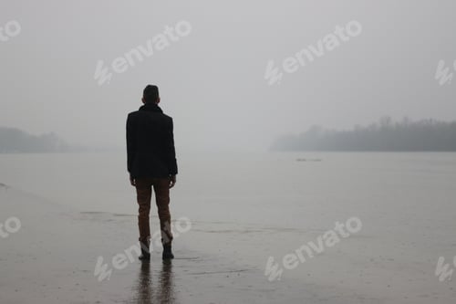 Preview: Man standing on the side of a river while raining