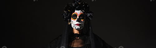 Preview: portrait of woman in sugar skull makeup and dark wreath looking at camera isolated on black, banner